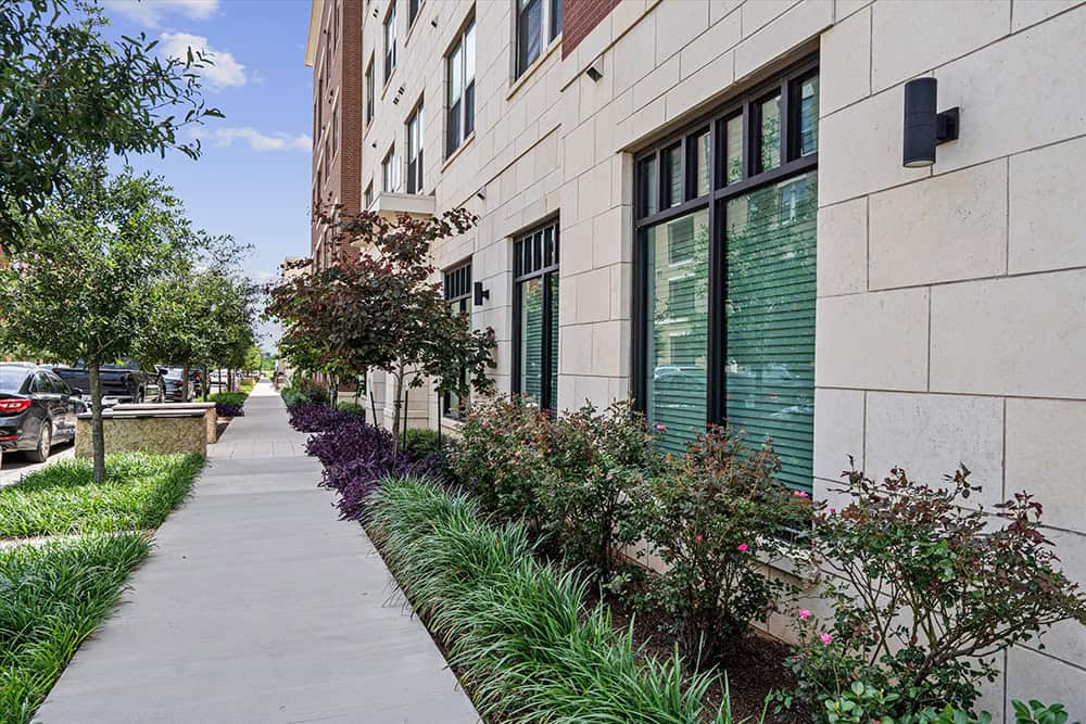 Modern residential building with landscaped sidewalk and greenery.