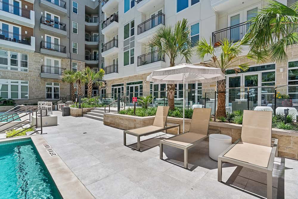 Modern apartment complex poolside with lounge chairs and palm trees.